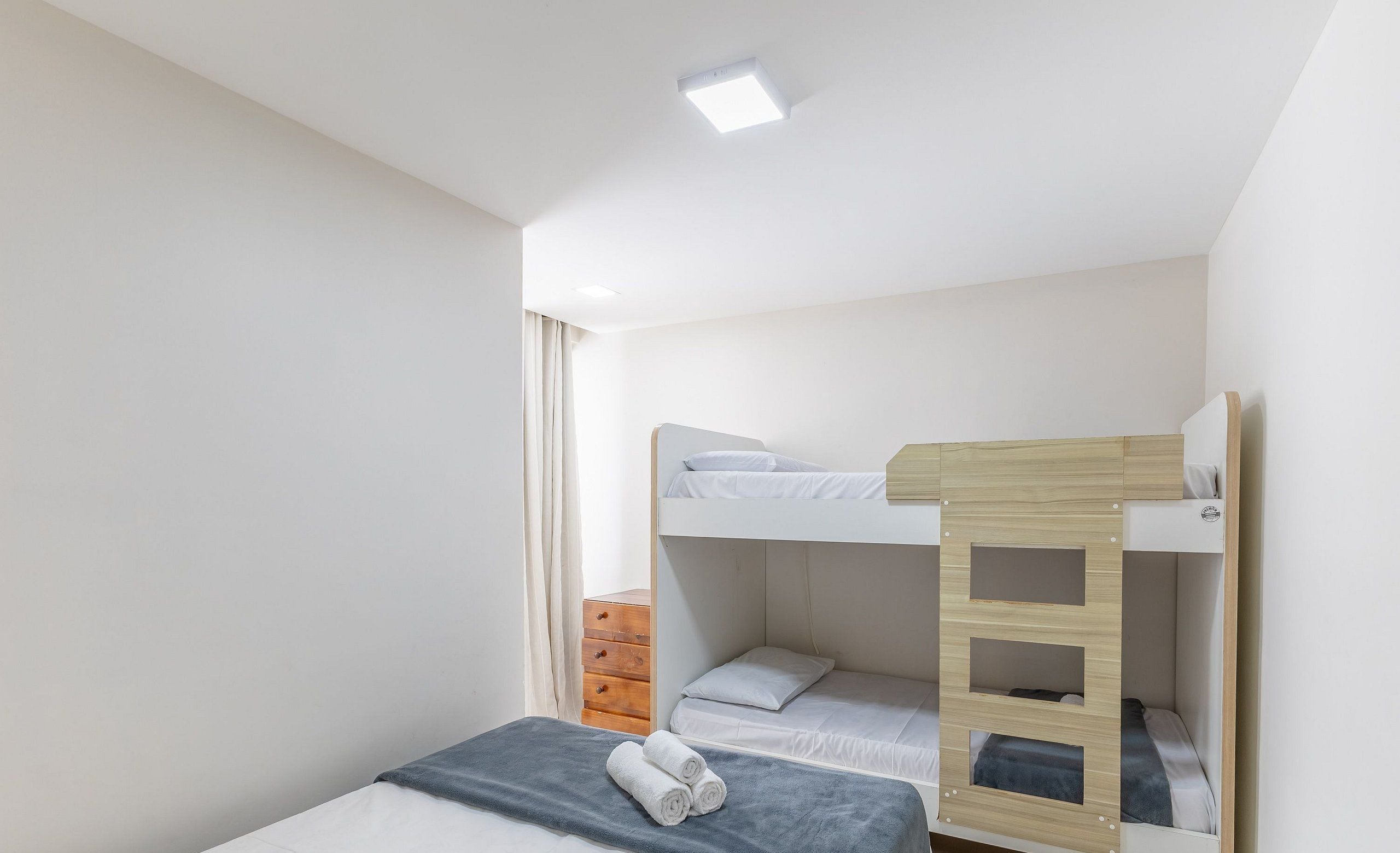 A bunk bed room with a single bed, a wooden ladder, and a dresser.