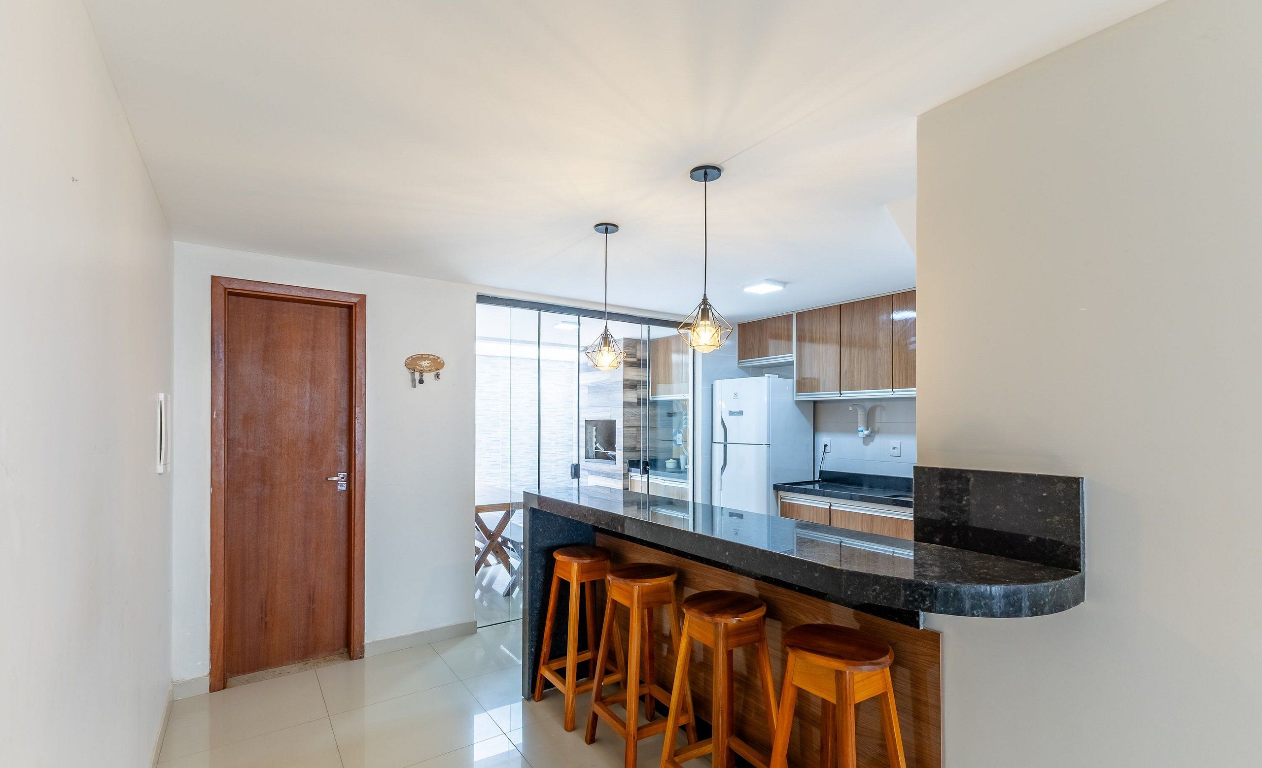 Cozinha moderna com bancada preta, banquetas de madeira e iluminação pendente.