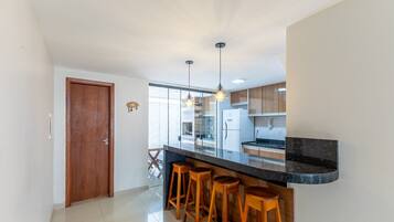 Cozinha moderna com bancada preta, banquetas de madeira e iluminação pendente.