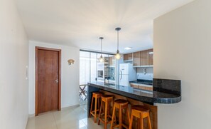 Una cocina moderna con encimera negra, taburetes de madera e iluminación colgante.