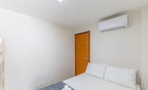 A bedroom with a bed, white bedding, an air conditioner, and a wooden door. - House w/ Terrace & BBQ 100m From the sea Ellc0000 (Ilhéus)