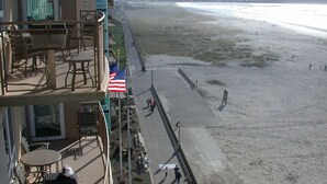 A beach view from a balcony with outdoor furniture and an American flag.