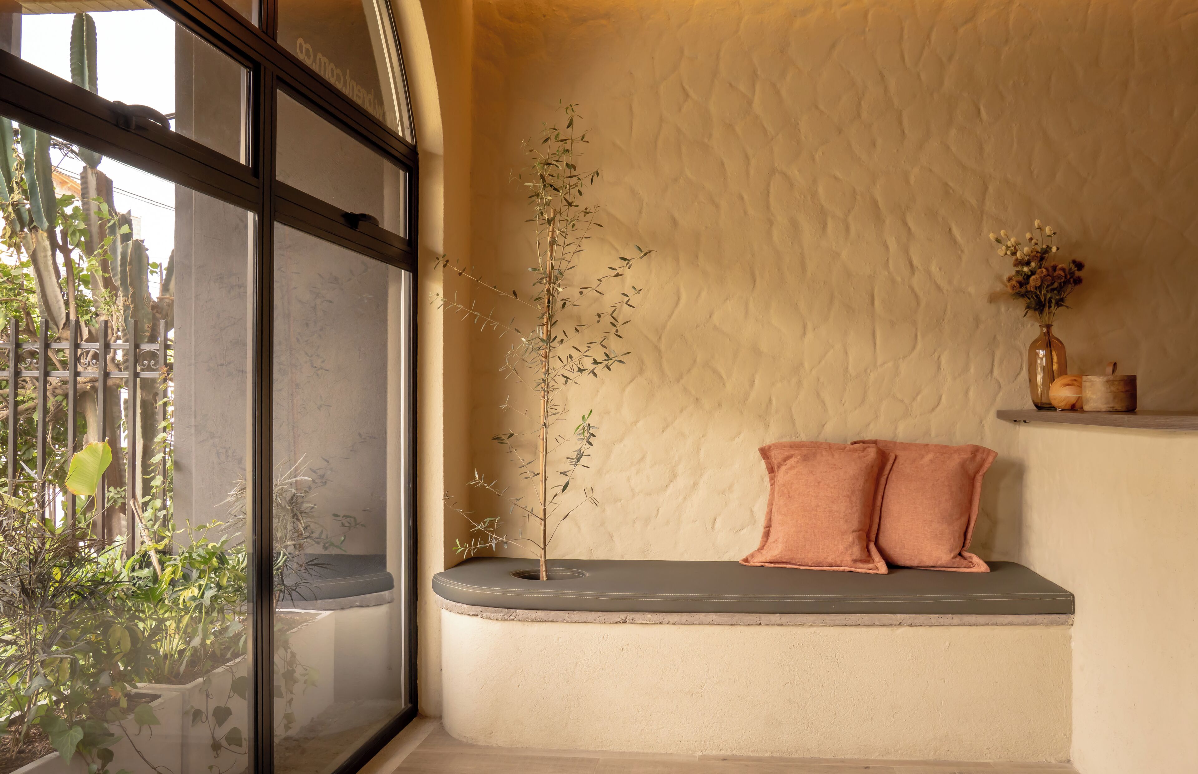 A room with a bench, a plant, and a vase with flowers.