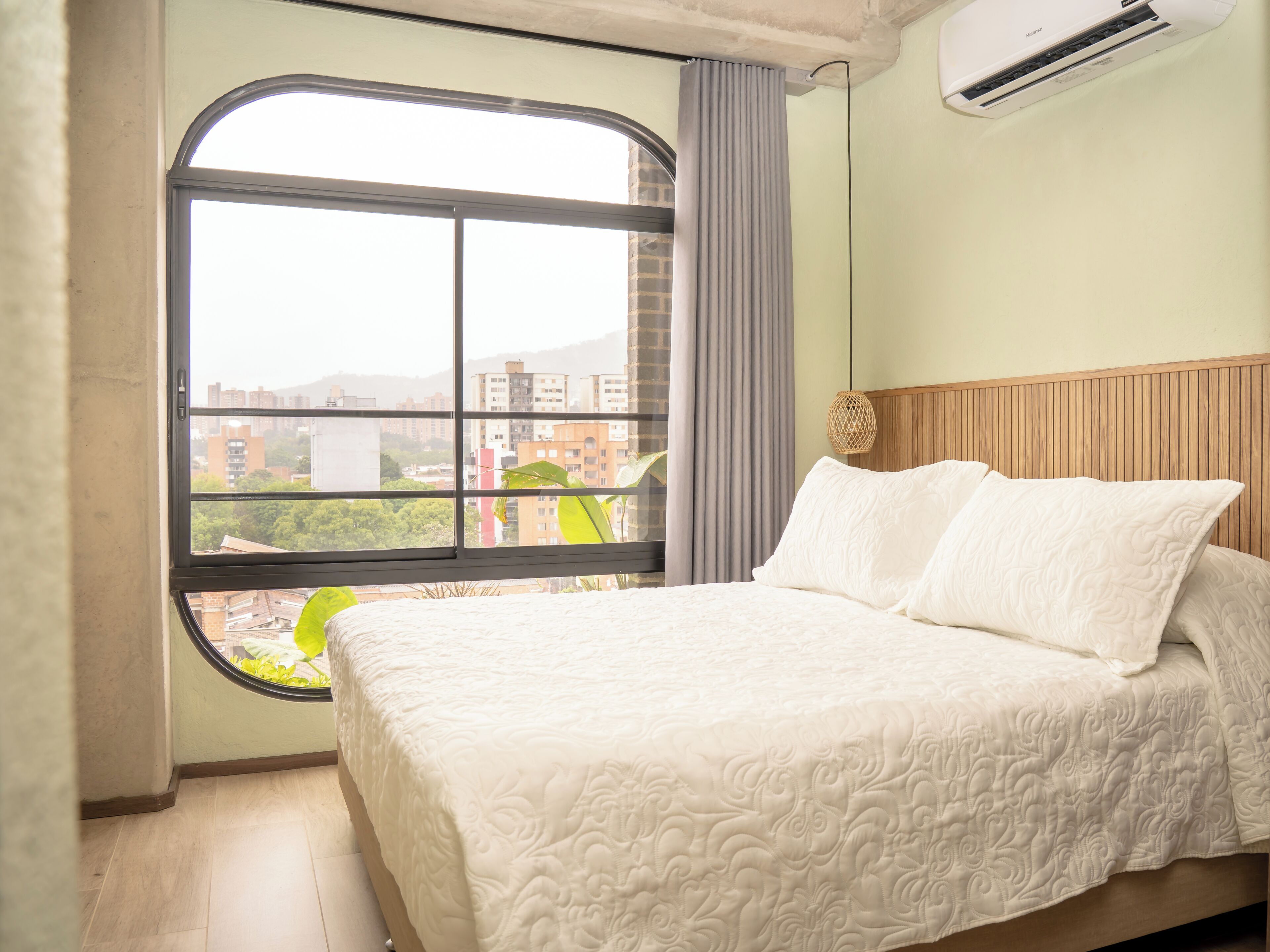 A hotel room with a large window, a bed with white bedding, and a wooden headboard.