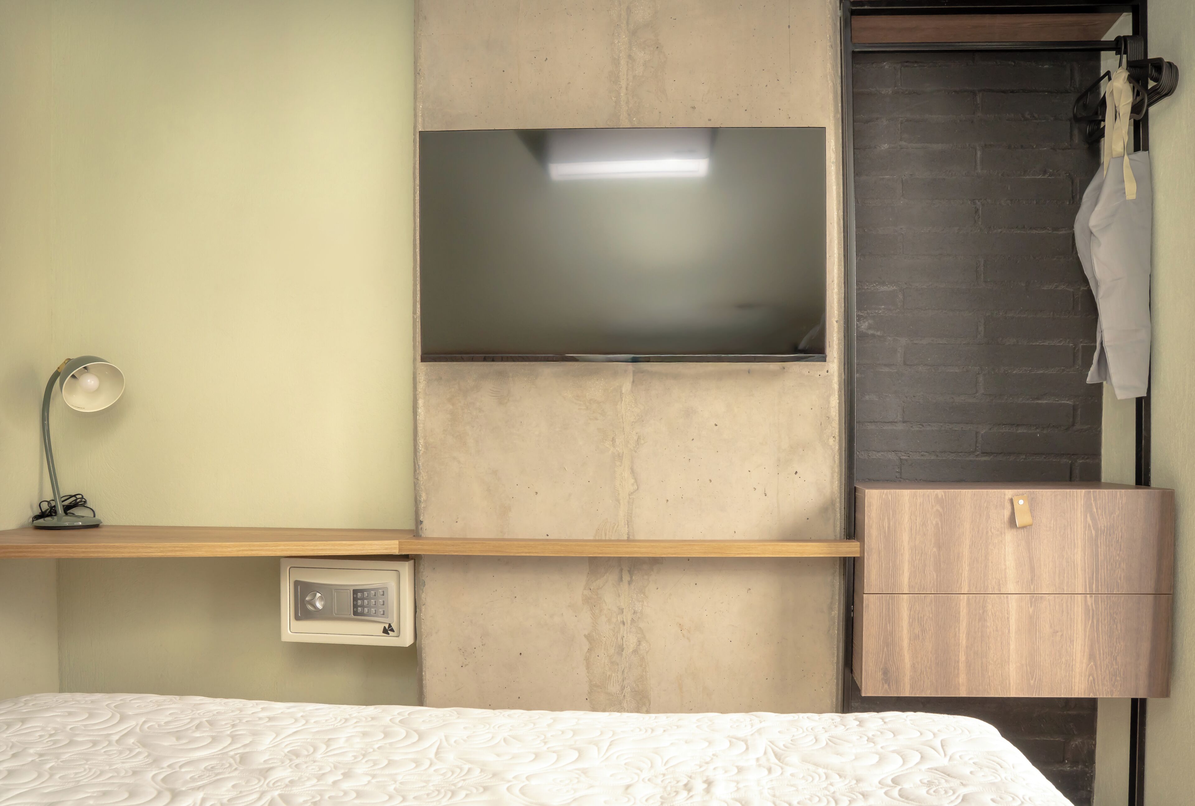 A bedroom with a bed, a TV mounted on a wall, a bedside table with a lamp, and a wooden cabinet.