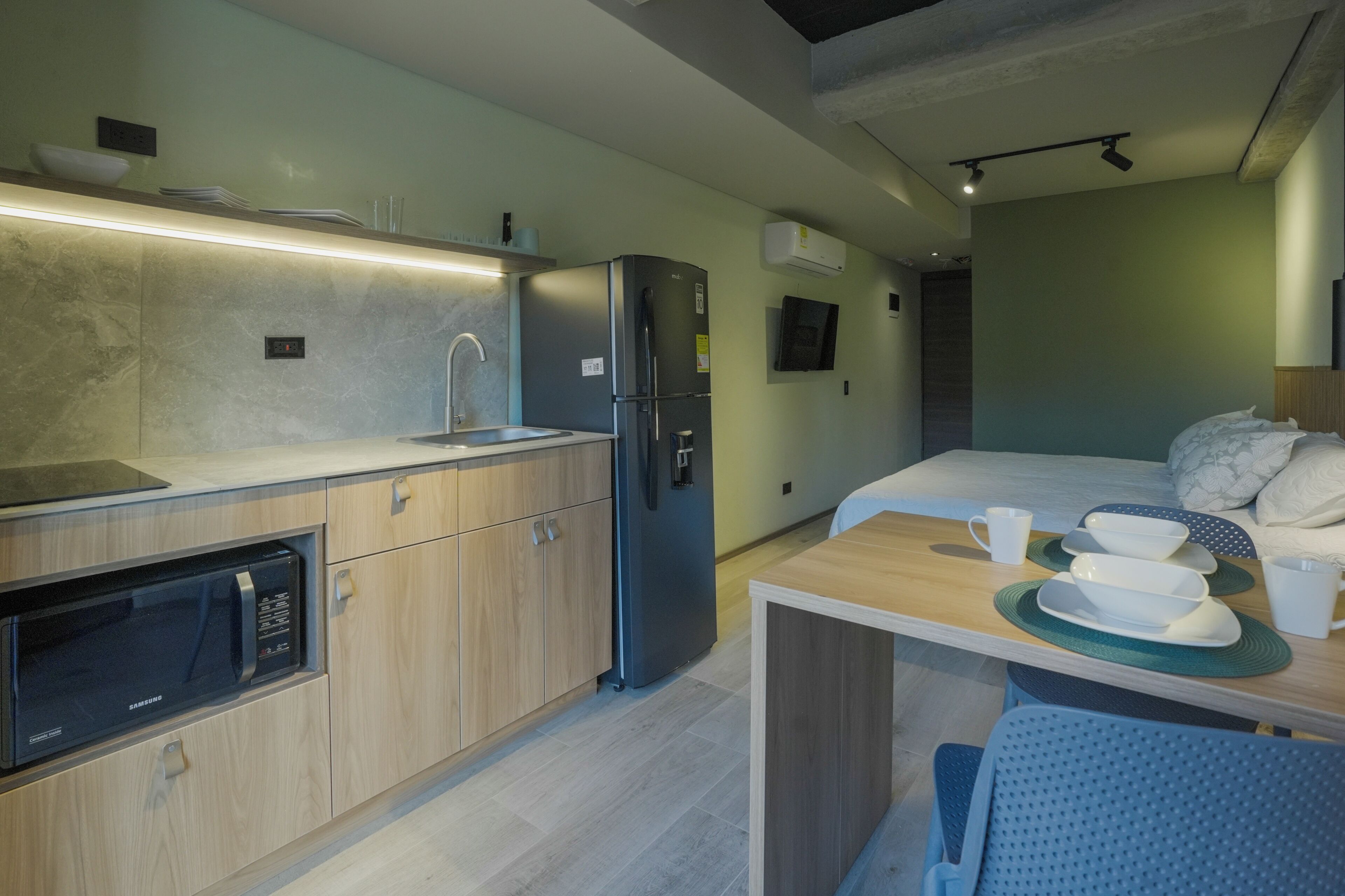 A compact hotel room with a kitchenette, a bed, and a small dining area.