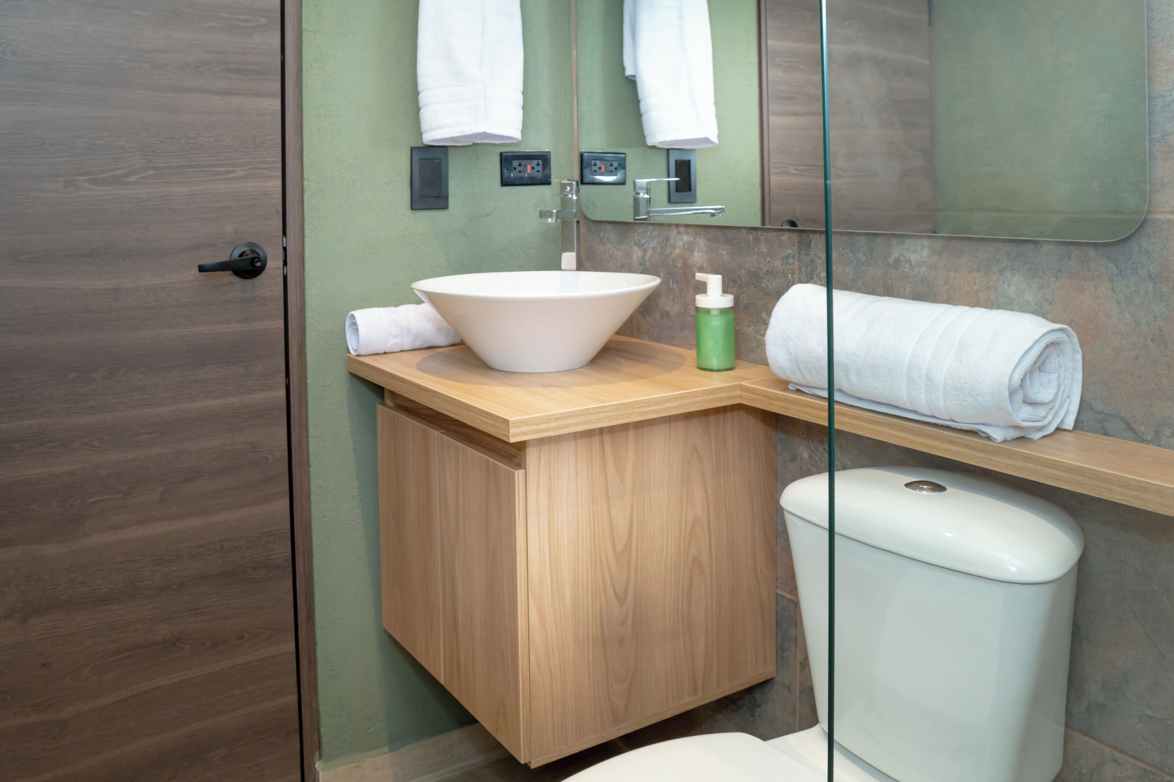 A bathroom with a wooden vanity, a white sink, a toilet, and a glass shower enclosure.
