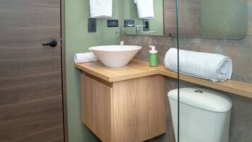 A bathroom with a wooden vanity, a white sink, a toilet, and a glass shower enclosure.