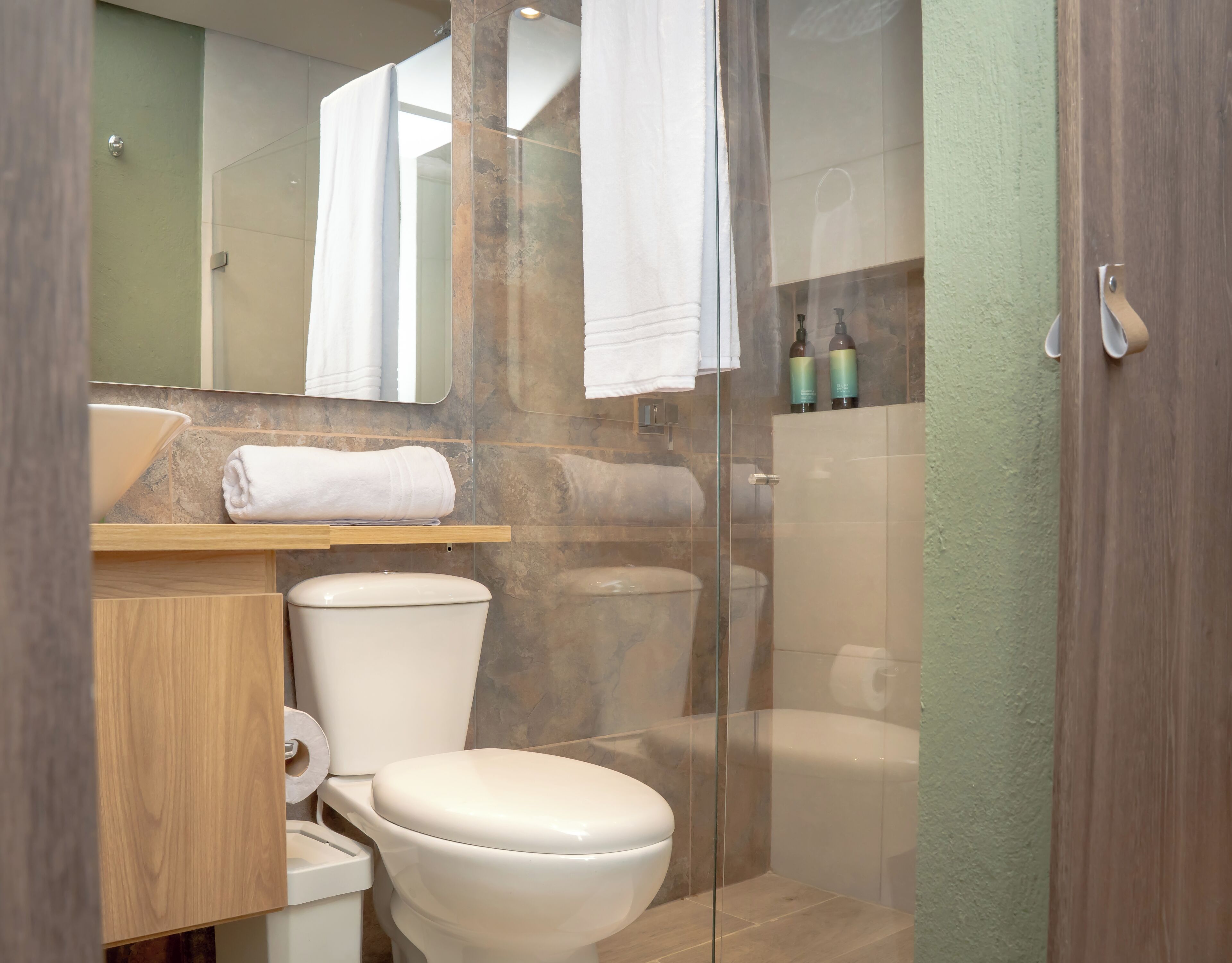 Ein Badezimmer mit Toilette, einer Glasdusche, einem Waschbecken mit Spiegel und einem Handtuchhalter.