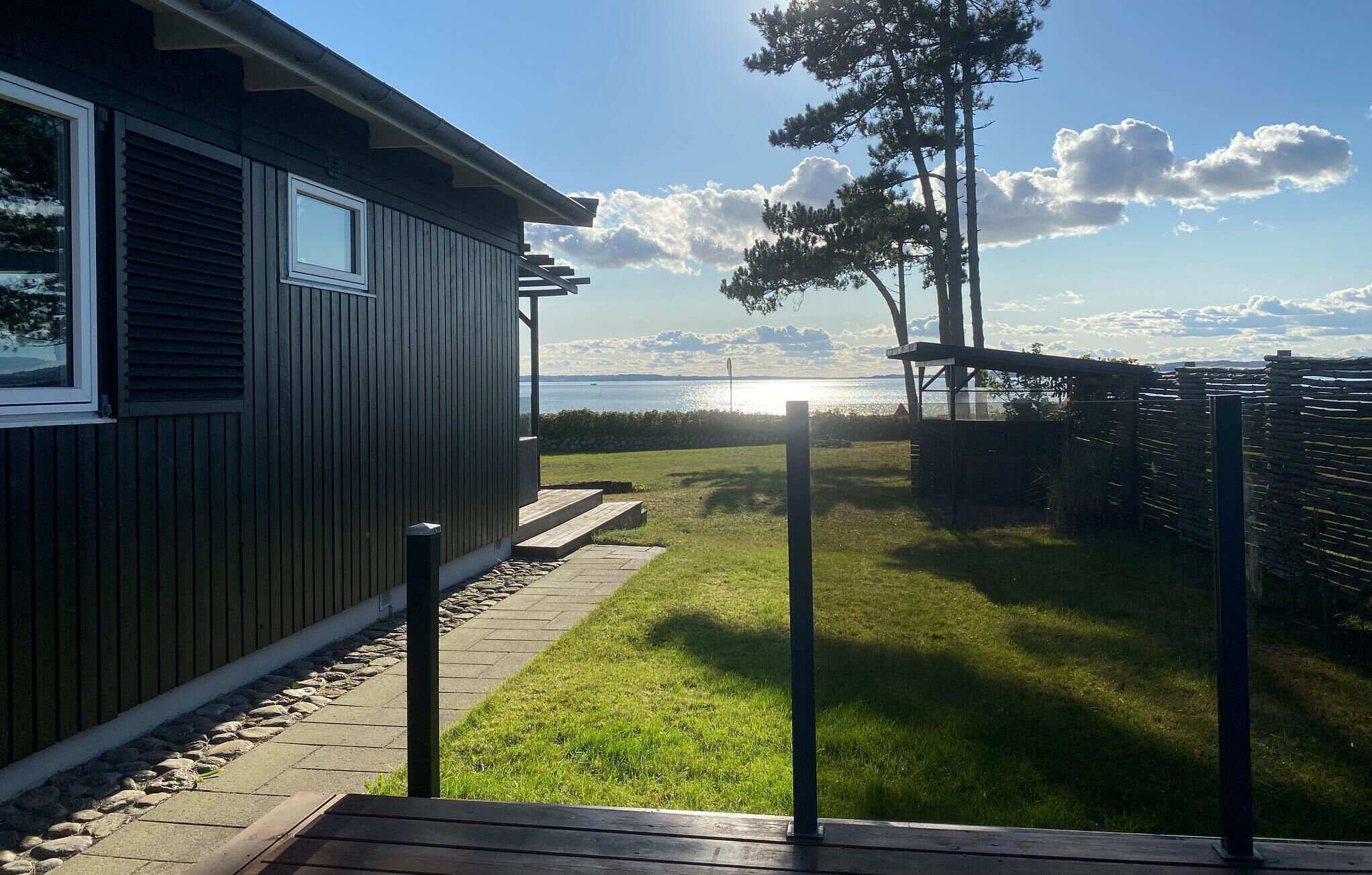 Una casa con un porche, un patio con césped y vista al mar.