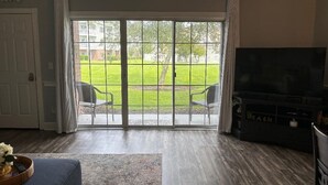 Una sala de estar con puerta corrediza de vidrio que da a un patio trasero. A la derecha hay un televisor y un sofá azul en el centro.