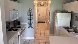 Una cocina estrecha con gabinetes blancos, estufa, microondas y refrigerador.