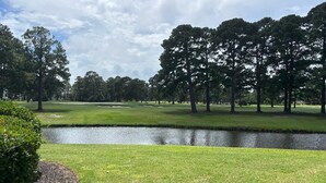 Un campo de golf con un estanque, árboles y un cielo despejado.
