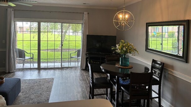 Una sala de estar con televisor, una mesa de comedor con sillas, una araña y un ventanal con vistas a un jardín.