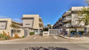 Un immeuble d’appartements moderne doté d’une entrée sécurisée par un portail, de nombreux balcons et d’une allée pavée.