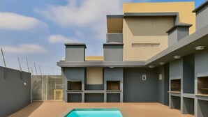 Un bâtiment moderne doté d’une piscine, avec une façade aux couleurs gris et beige, et un ciel dégagé.