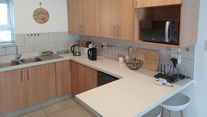 Une cuisine avec des meubles de rangement en bois, un évier, un four à micro-ondes et un plan de travail sur lequel sont disposés divers ustensiles de cuisine.