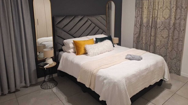 Une chambre moderne avec un grand lit, une table de chevet, un miroir et des rideaux à motifs.