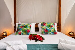 A bed with white linens, two floral pillows, a bouquet of red flowers, and a teal throw blanket. - Canopée 5-stars, bay view, terrace, CANOPÉE, Votre Parenthèse Céleste (Les Trois-Îlets)