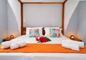 Ein ordentlich bezogenes Bett mit weißen Bettwäsche, zwei farbenfrohe Kissen, eine rote Blume und zwei Nachttischlampen.