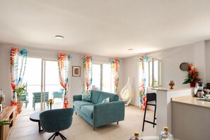 A living room with a sofa, chairs, a coffee table, and a kitchen area with a counter and appliances. - Canopée 5-stars, bay view, terrace, CANOPÉE, Votre Parenthèse Céleste (Les Trois-Îlets)