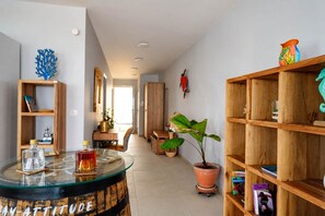 A modern living room with a glass coffee table, wooden bookshelves, a potted plant, and a wooden cabinet. - Odyssée 5 stars, 2 suites, bay view, ODYSSÉE, Votre Parenthèse Céleste (Les Trois-Îlets)