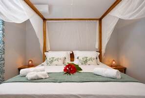 A neatly made bed with white linens, a green throw blanket, and decorative pillows with a leaf pattern. There are two bedside lamps with a patterned shade. - Odyssée 5 stars, 2 suites, bay view, ODYSSÉE, Votre Parenthèse Céleste (Les Trois-Îlets)