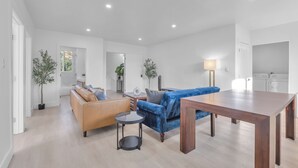 Een ruime woonkamer met een bank, een blauwe bank, een ronde tafel en een houten eettafel.