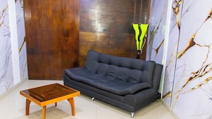 Ein Zimmer mit einem dunkelgrauen Sofa, einem Holztisch und einer Wand mit Marmoroptik.