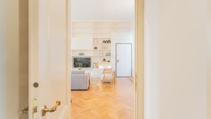 Een geopende deur die leidt naar een woonkamer met een bank, televisie en houten vloer.