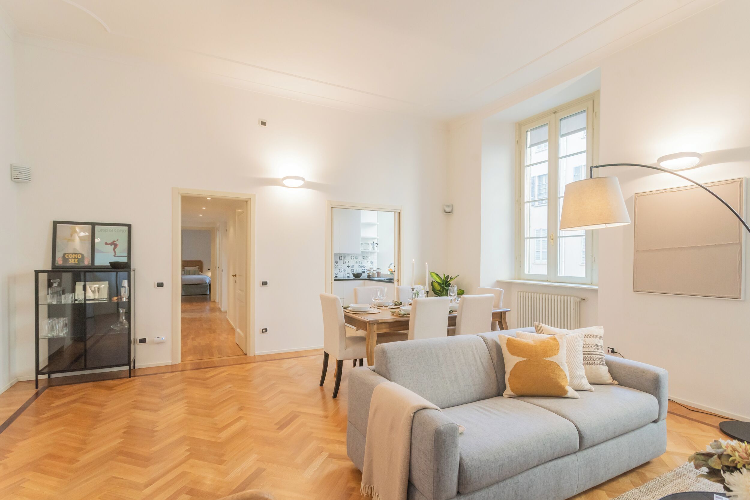 Ein geräumiger Wohnbereich mit grauem Sofa, einem Esstisch und einer Küche im Hintergrund.
