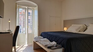 Une chambre à coucher avec un lit, un bureau et une chaise. Il y a une fenêtre qui donne sur les bâtiments à l’extérieur.