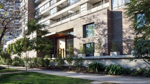 A modern multi-story building with balconies, large windows, and a well-maintained garden area.