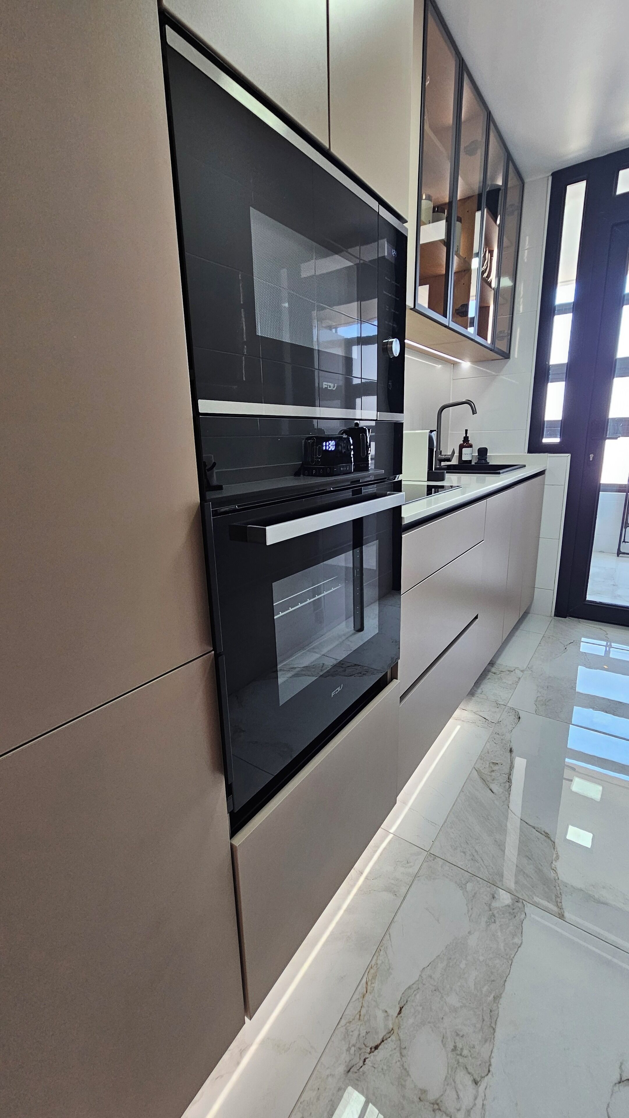 A modern kitchen with a built-in oven and microwave, a stainless steel sink, and a large window providing natural light.