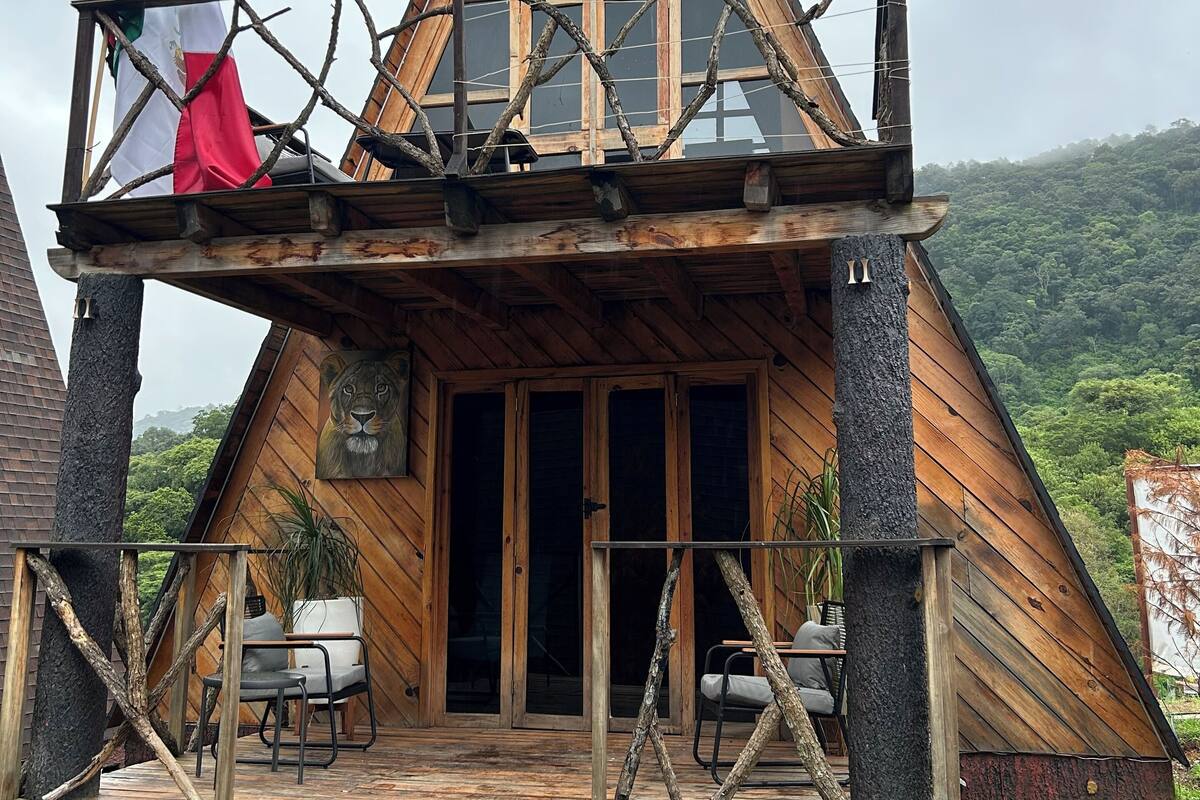 Una cabaña de madera triangular con balcón, un cuadro de león y una bandera.