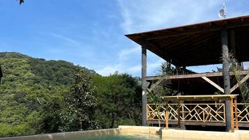 Área de piscina com deck de madeira e vista para um morro verdejante.