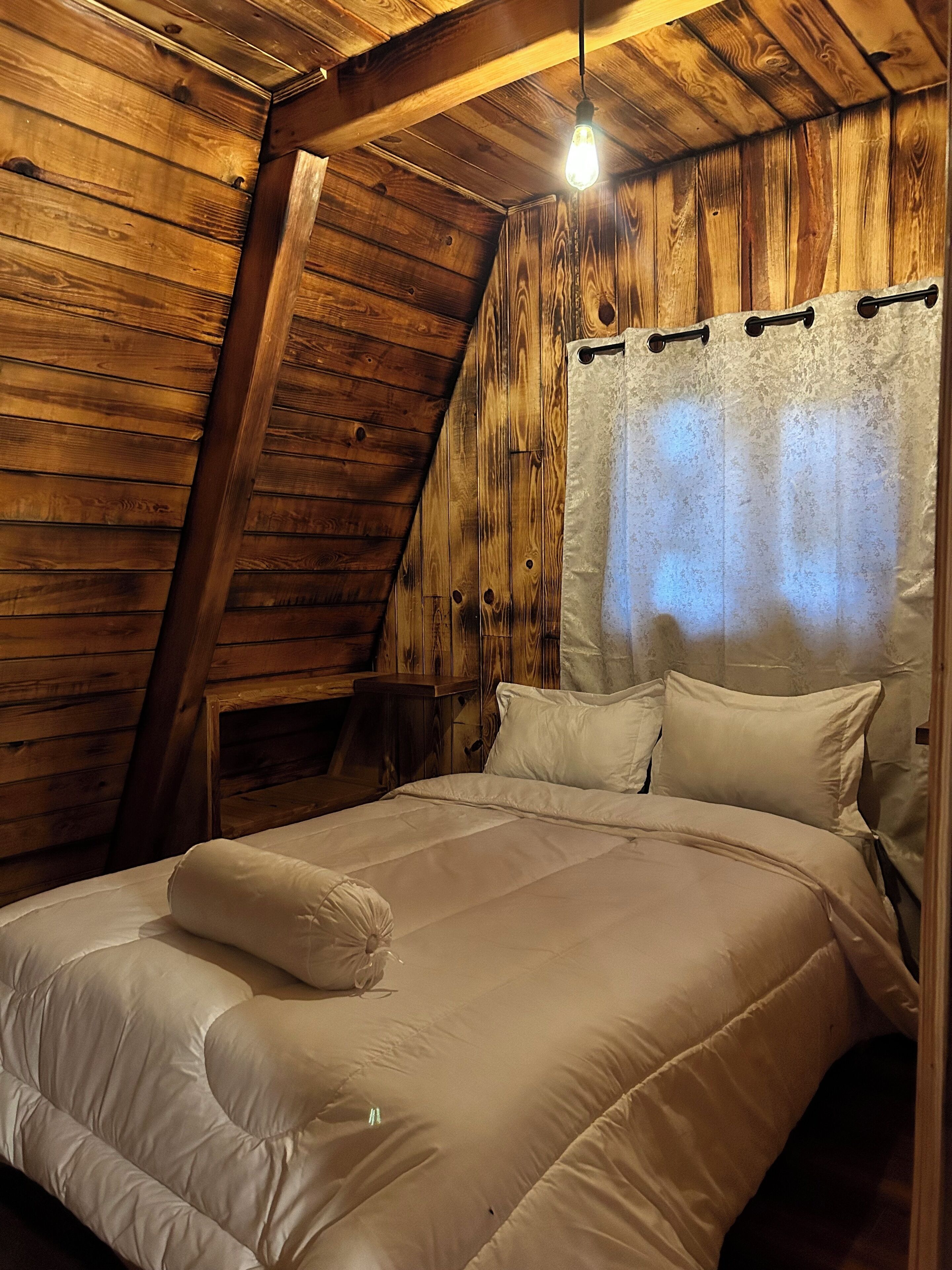 Un dormitorio con techo inclinado, paredes de madera, una cama con ropa blanca y una lámpara colgante.
