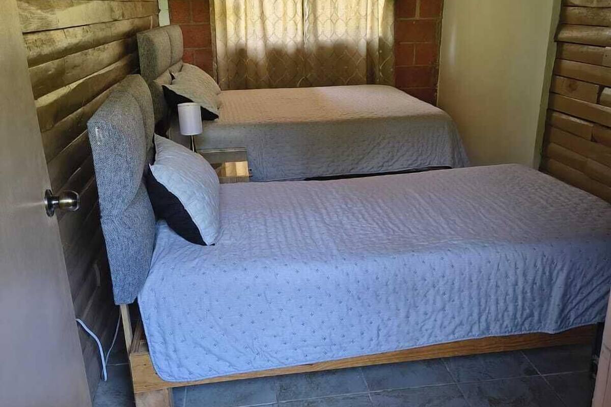 Habitación pequeña con dos camas, una mesita y una ventana con cortinas.