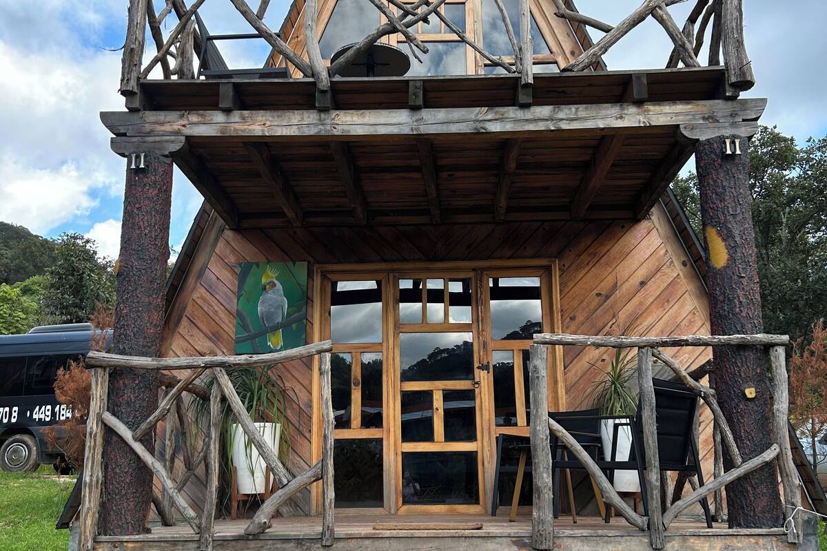 Una cabaña de madera con techo triangular, un balcón y una escalera que lleva a la entrada.