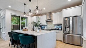A modern kitchen with a central island, bar stools, stainless steel appliances, and pendant lighting. - Spacious 5BR Central Austin Home w/Pool, Sleeps 13 (Austin)