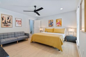 Ein Hotelzimmer mit einem Bett, einem grauen Sofa, einem Nachttisch und einem Deckenventilator.