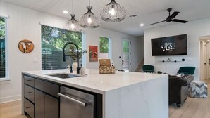 A modern kitchen with a large island, stainless steel appliances, pendant lighting, and a flat-screen TV mounted on the wall. - Spacious 5BR Central Austin Home w/Pool, Sleeps 13 (Austin)