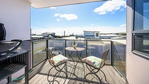 Un balcon avec un barbecue, deux chaises et une table sur laquelle se trouve une bouteille.