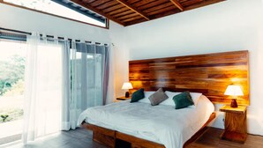 Ein großes Bett mit Holz Kopfteil, zwei Nachttischlampen und Blick auf Grünflächen.