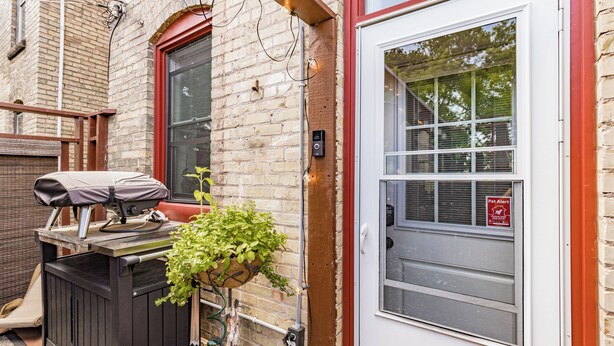 A brick building with a wooden deck, a barbecue grill, and a potted plant. - Nostalgia Nook - Vintage Studio (Duluth)