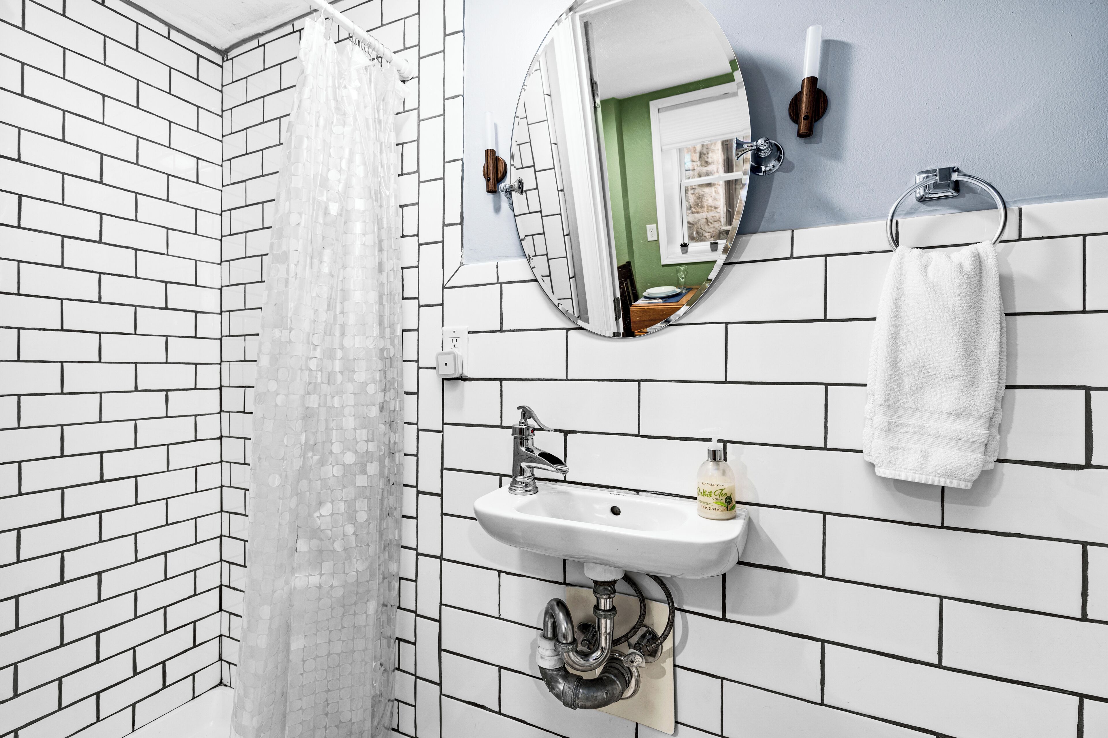 Een badkamer met witte baksteenmuren, een witte wastafel, een spiegel en een handdoekhouder.