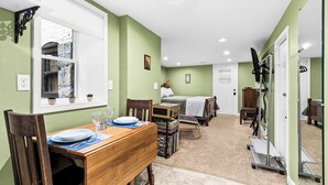 A room with a dining table set for two, a bed, a small table with a chair, and a mirror. - Nostalgia Nook - Vintage Studio (Duluth)