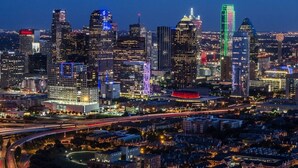 A city skyline at night with illuminated buildings and a highway.