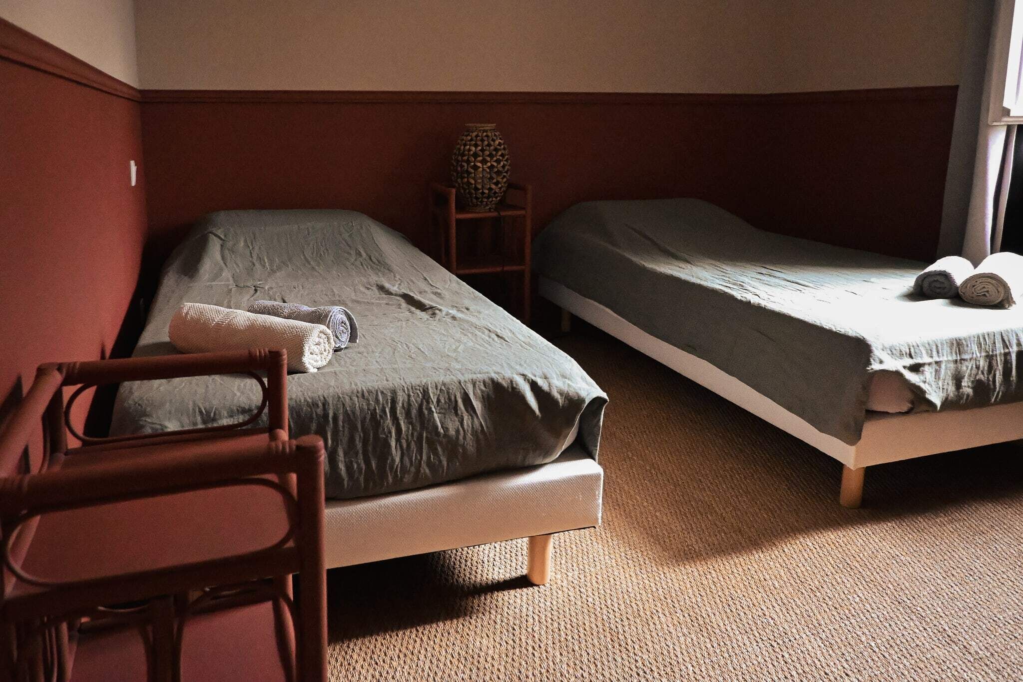 A room with two single beds, a wooden chair, and a small table with a vase.
