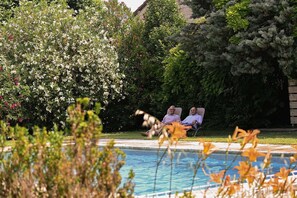 Two people seated by a pool with lush greenery and a stone wall in the background. - Le Mas de la Digue - Provence (Châteaurenard)